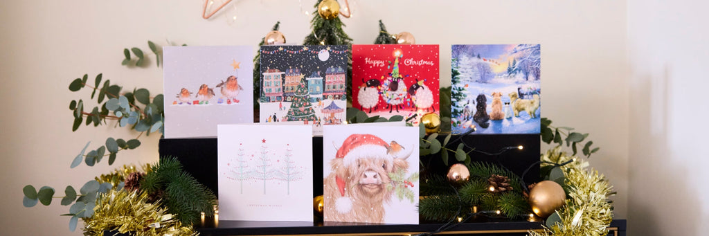 A collection of various Christmas cards on a mantelpiece, decorated with tinsel and foliage.