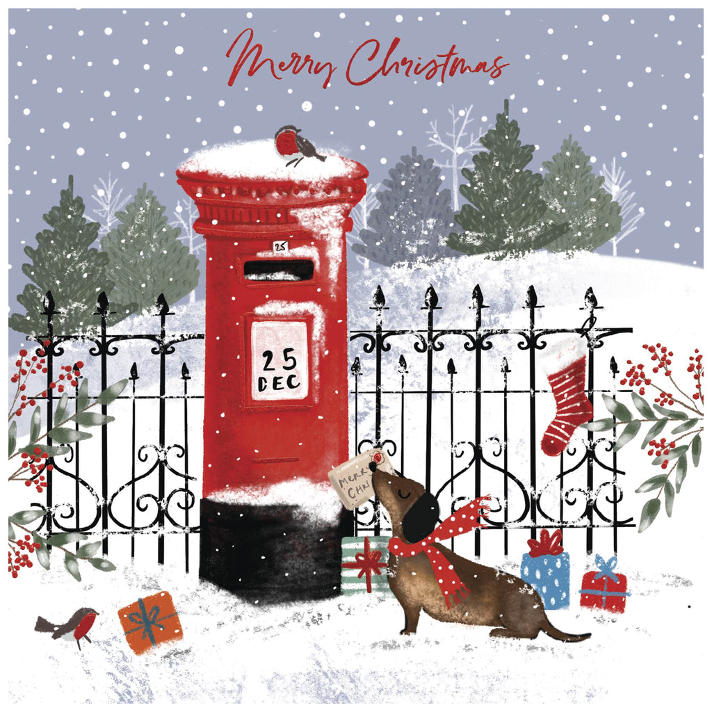 A Christmas card of a festive snowy scene featuring a red postbox with '25 DEC' written on it, topped with a small bird. A dachshund wearing a red scarf stands on its hind legs, holding an envelope addressed to 'North Pole' in its mouth. In front of the postbox is a black wrought iron fence decorated with holly and a hanging red stocking. Evergreen trees and a snowy landscape form the background, with wrapped presents scattered on the snow. The text 'Merry Christmas' appears at the top in red cursive.