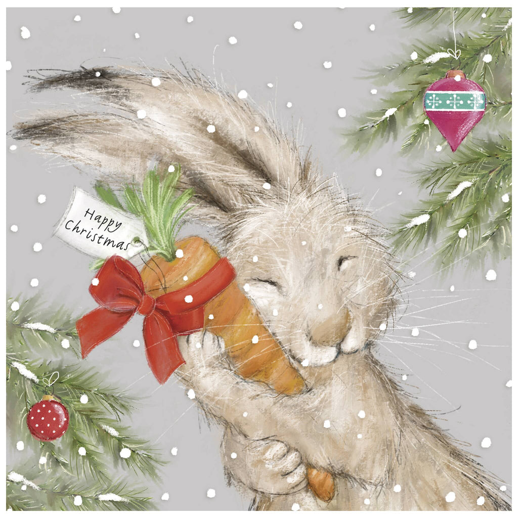 A Christmas card of a rabbit hugging a large carrot tied with a red ribbon and a tag that reads 'Happy Christmas'. Snow falls in the background, with decorated Christmas tree branches and ornaments adding to the festive scene.