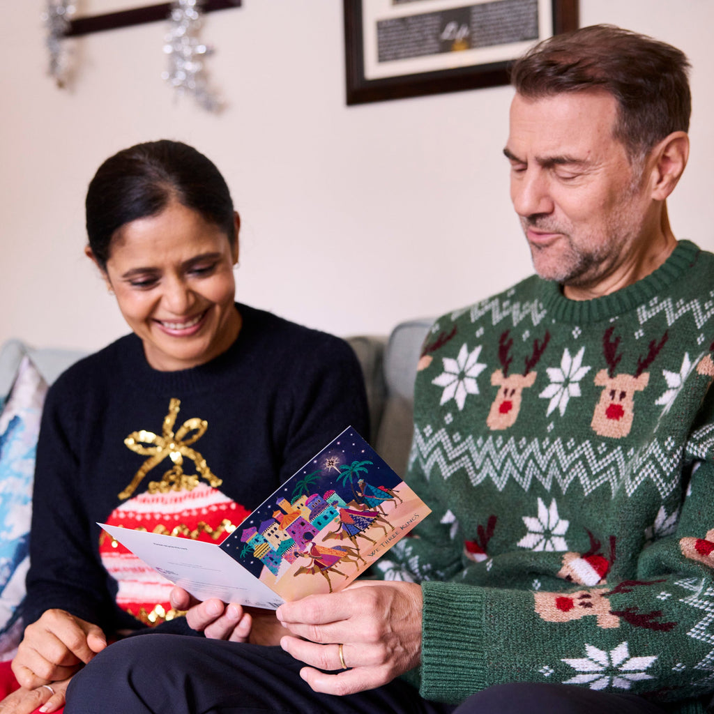 A couple read the inside of a Cancer Research UK Three Kings Christmas Card. A religious Christmas card design.