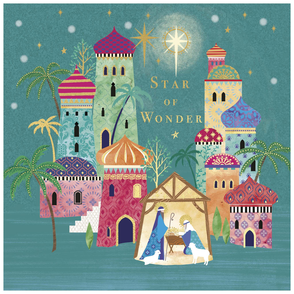 A Christmas card of a colourful, stylised nativity scene with Mary and Joseph beside baby Jesus in a manger under a stable. Two sheep rest nearby, and the background features vibrantly patterned buildings with domed roofs in red, green, blue, and yellow. Palm trees are scattered throughout, and a bright star with golden rays shines above the stable. The words 'STAR OF WONDER' appear in gold to the right of the star.