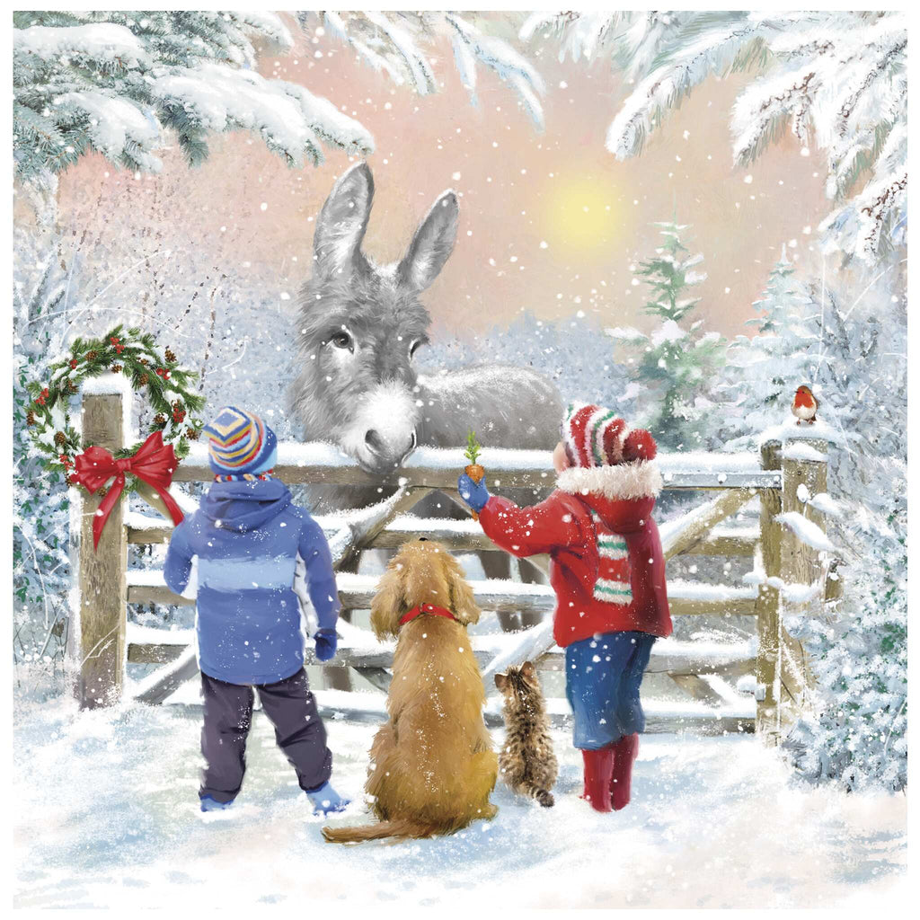 A Christmas card of two children in winter clothing standing with a dog and a cat in front of a snow-covered wooden gate, interacting with a donkey peering over it. One child offers food to the donkey. The gate is decorated with a wreath and red ribbons, and snow falls gently over the wintry landscape of trees and ground