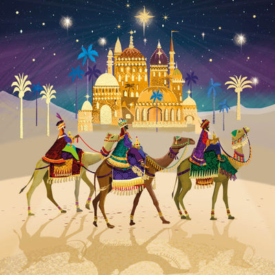 Traditional Christmas card featuring an illustrated scene of three camels with kings riding traveling toward a golden palace under a starry night sky, with palm trees and a desert landscape.