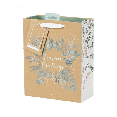 A Christmas kraft paper gift bag with a hanging tag, decorated with watercolor eucalyptus leaves in muted blue-green and gold tones, and the words 'Season's Greetings' on the front. The side panel features a white background with a matching botanical pattern.
