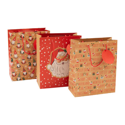 Three Christmas-themed paper gift bags on a plain white background. One bag has a gold background with gnome illustrations, one is red with white polka dots and a Santa Claus graphic, and one is tan with repeated 'Jolly Jolly Christmas' text and a red heart-shaped handle.