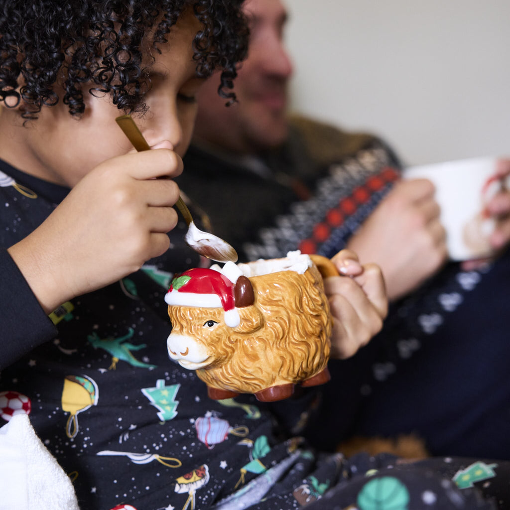 A boy spoons for marshmallows out of his Highland Cow Christmas Mug