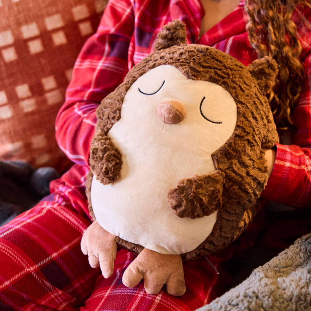 Novelty extra large owl hand warmer. Designed with comfort in mind, this huggable hand warmer is perfect for autumns rain and winters cold. Simply slide your hands into either pocket and snuggle away! In this image, a girl is using the owl hand warmer.