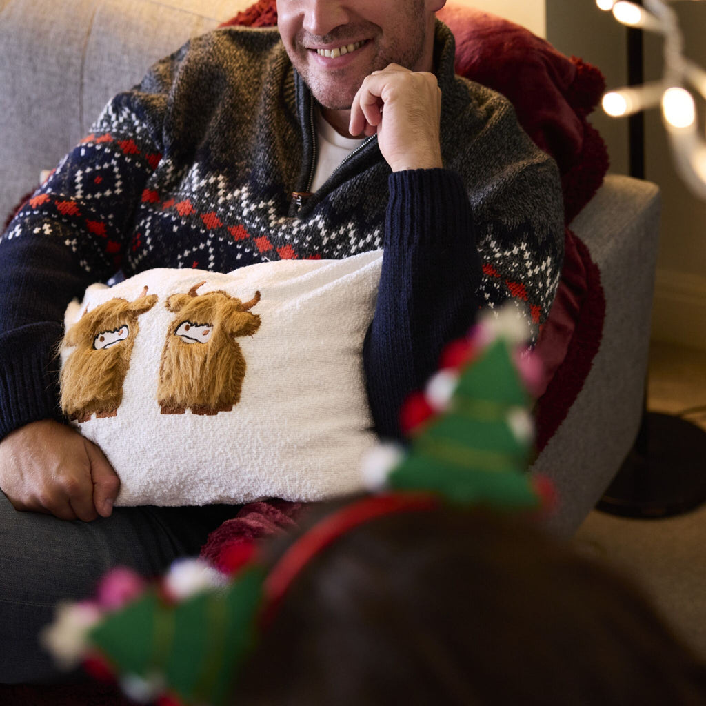Highland Cow applique cushion. Man snuggles up to the soft cushion while sitting on a sofa.