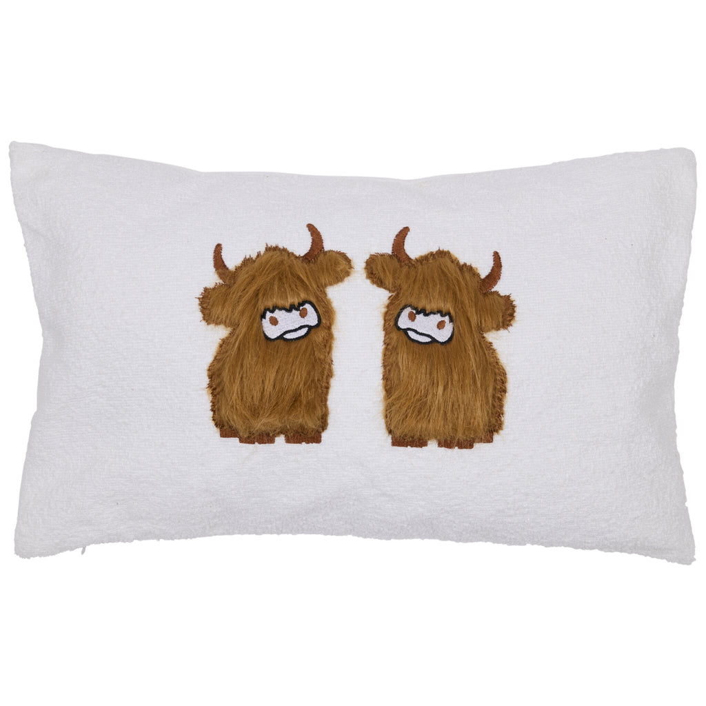 Highland cow applique cushion. White cushion featuring two embroidered brown highland cows with horns and white faces, standing side by side in the center.