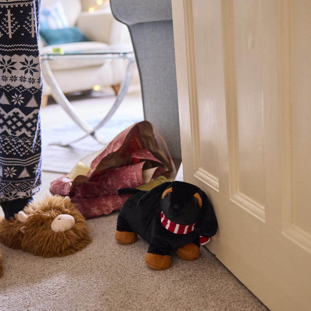 Dinky Dachshund Door stop is propped up again a door. 