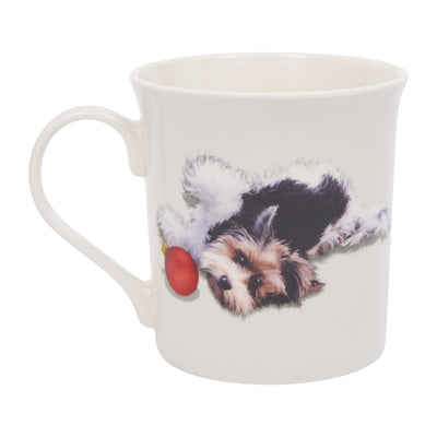 A white ceramic mug featuring a printed illustration of a small black and white dog playing with a red bauble.
