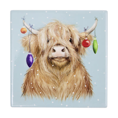 A square ceramic tile coaster featuring a detailed illustration of a fluffy Highland cow with white horns decorated with hanging Christmas baubles, set against a light blue snowy background.