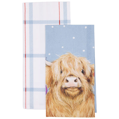Two kitchen towels shown on a white background: one with a white base, light blue plaid pattern, and red dashed edge stripes; the other featuring a fluffy tan Highland cow illustration on a light blue background with white speckles.