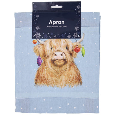 A light blue kitchen apron with a printed illustration of a fluffy Highland cow decorated with hanging Christmas ornaments.