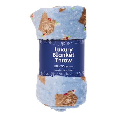 A light blue plush fleece blanket with a brown Highland cow and Christmas holly pattern, wrapped in a dark blue paper band labeled 'Luxury Blanket Throw'.