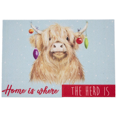 A square door mat featuring a fluffy Highland cow illustration on a light blue snowy background, with hanging ornaments and the text 'Home is where THE HERD IS' at the bottom.