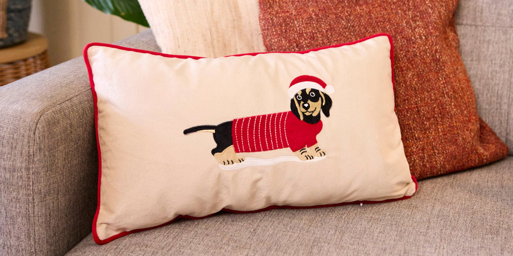 A Christmas dachshund cushion is placed on a sofa.