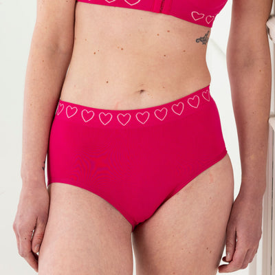 Woman wearing Cancer Research UK comfort brief in hot pink, showing supportive fit and smooth finish.