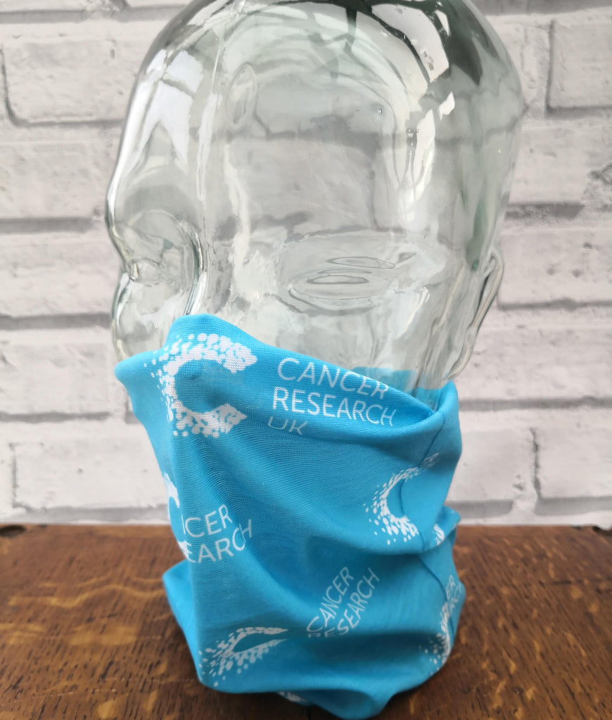 Blue multifunctional snood with Cancer Research pattern displayed on a mannequin head, styled as a face covering. Ideal for post-chemo recovery, with soft, breathable fabric that won’t irritate sensitive skin.
